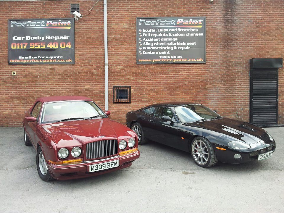 A burgundy Bentley and a black Jaguar XKR parked outside the Perfect Paint unit under the signs