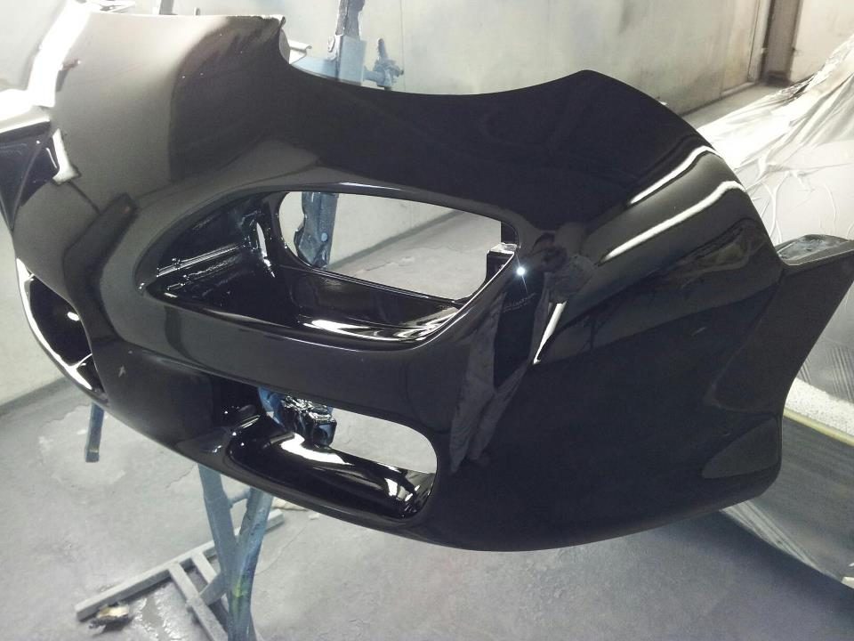 A front bumper painted gloss black on a stand in the booth