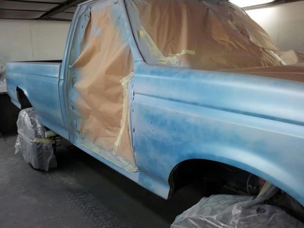 The pickup in blue primer with its windows and wheels masked in brown paper