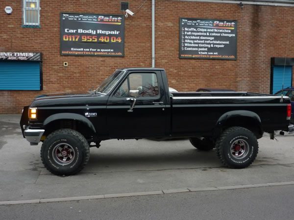 The finished black pickup parked outside the Perfect Paint unit and its signs