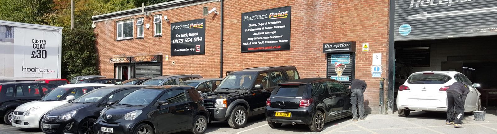 The Perfect Paint unit on Crews Hole Road: red brick, black signs, cars lined up and the team at work by the open booth door